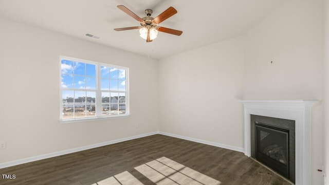 unfurnished living room with dark wood-style flooring, visible vents, a ceiling fan, a glass covered fireplace, and baseboards