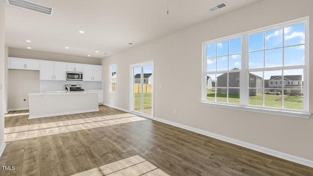 kitchen featuring a center island with sink, light countertops, stainless steel microwave, visible vents, and white cabinetry