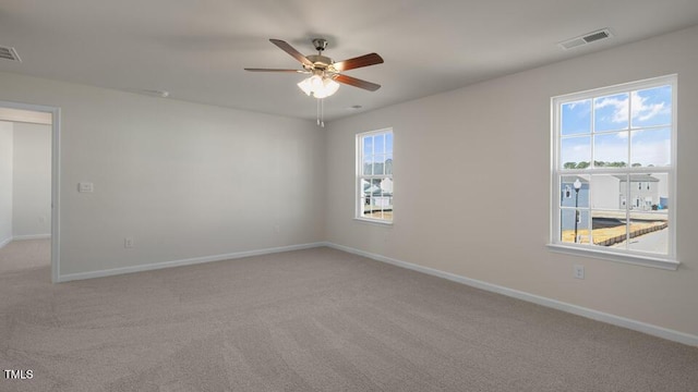 spare room with light carpet, a ceiling fan, visible vents, and baseboards