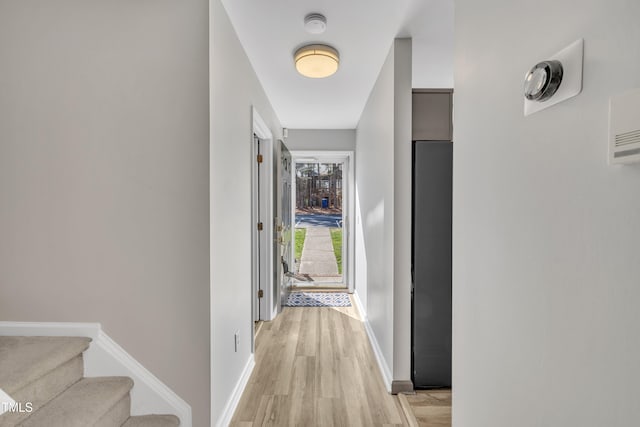 hall with stairway, light wood-type flooring, and baseboards