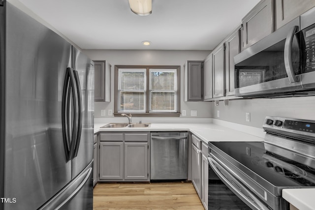 kitchen with light countertops, light wood-style flooring, gray cabinetry, appliances with stainless steel finishes, and a sink