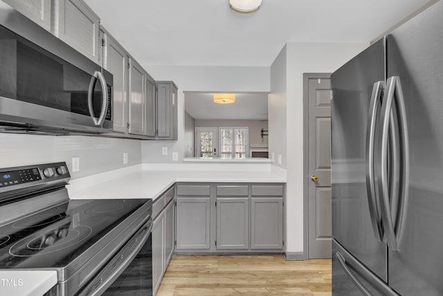 kitchen featuring stainless steel appliances, light wood-type flooring, light countertops, and gray cabinetry