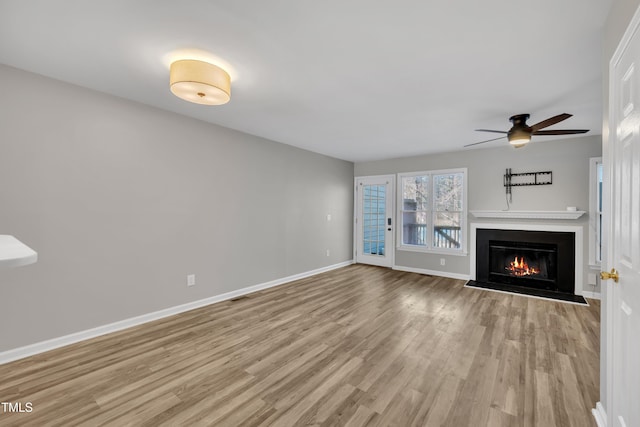 unfurnished living room featuring visible vents, light wood-style floors, a glass covered fireplace, ceiling fan, and baseboards