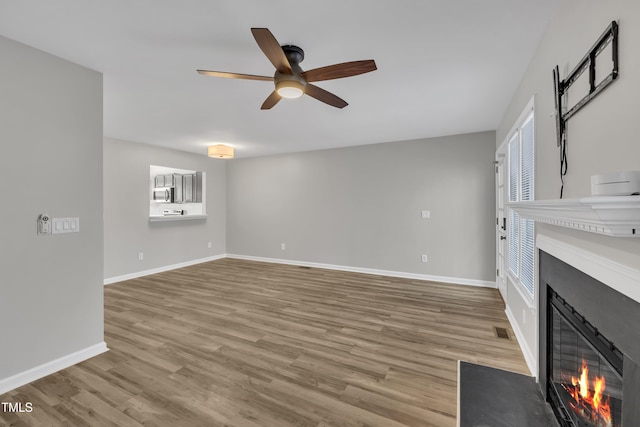 unfurnished living room with visible vents, baseboards, a fireplace with flush hearth, ceiling fan, and wood finished floors