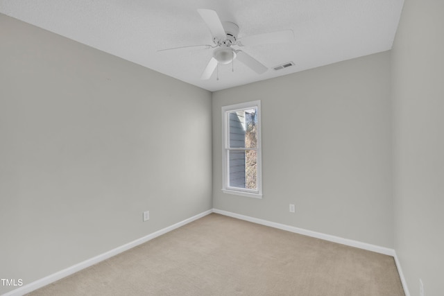 spare room with light colored carpet, visible vents, ceiling fan, and baseboards