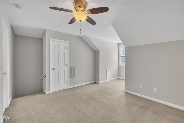 additional living space with baseboards, visible vents, lofted ceiling, a textured ceiling, and carpet flooring