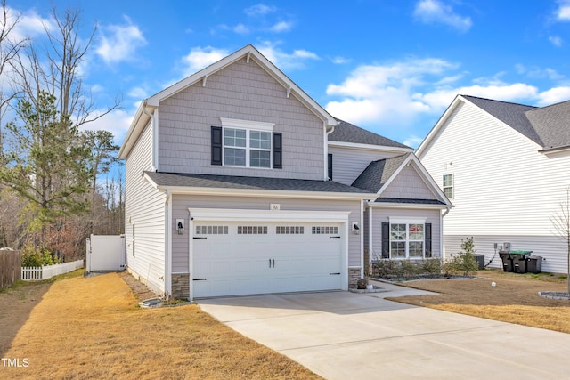 craftsman house featuring an attached garage, fence, driveway, stone siding, and a front lawn