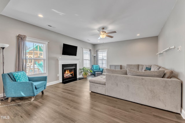 living room with a fireplace with flush hearth, plenty of natural light, wood finished floors, and visible vents