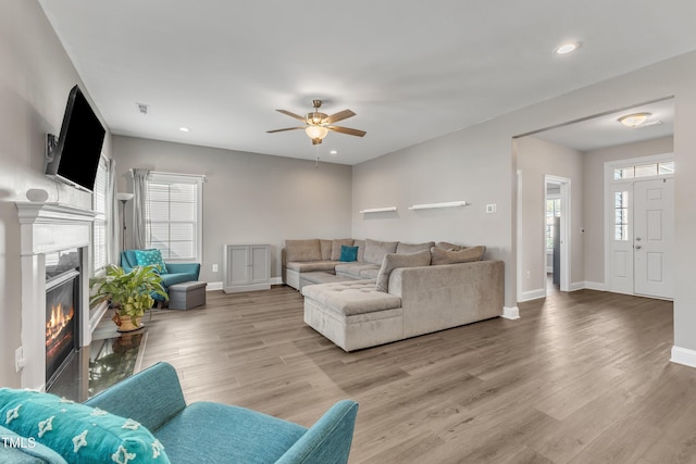 living room featuring a glass covered fireplace, baseboards, and light wood finished floors