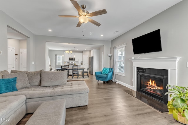 living area with a fireplace, recessed lighting, wood finished floors, baseboards, and ceiling fan with notable chandelier