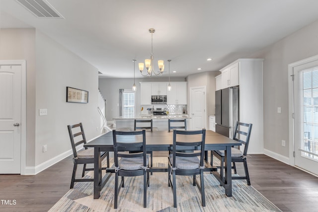 dining space featuring dark wood-style floors, a chandelier, visible vents, and baseboards