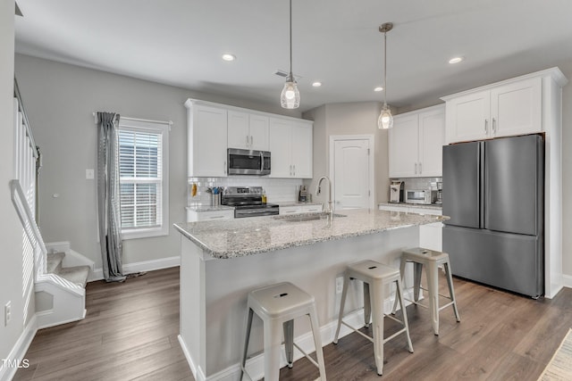 kitchen featuring stainless steel appliances, dark wood-type flooring, white cabinets, a sink, and a kitchen bar