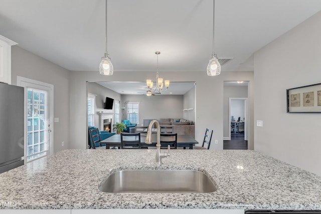 kitchen with a warm lit fireplace, open floor plan, a sink, and freestanding refrigerator