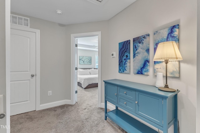 hallway with light colored carpet, visible vents, and baseboards