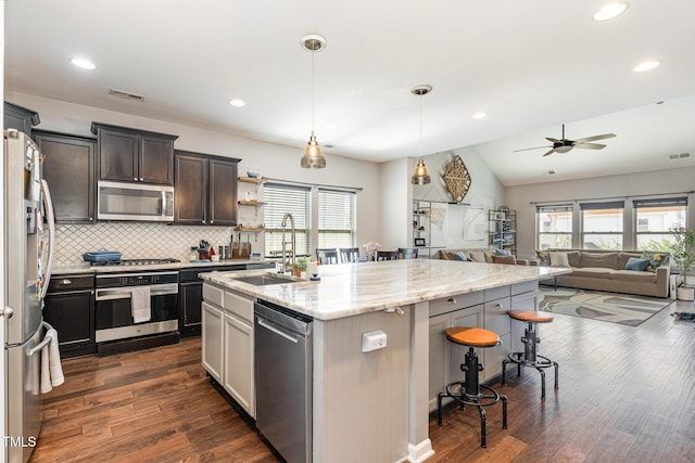 kitchen with a center island with sink, appliances with stainless steel finishes, hanging light fixtures, a kitchen bar, and a sink