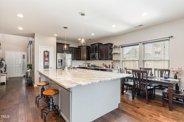 kitchen featuring a breakfast bar area, a spacious island, hanging light fixtures, appliances with stainless steel finishes, and dark brown cabinetry