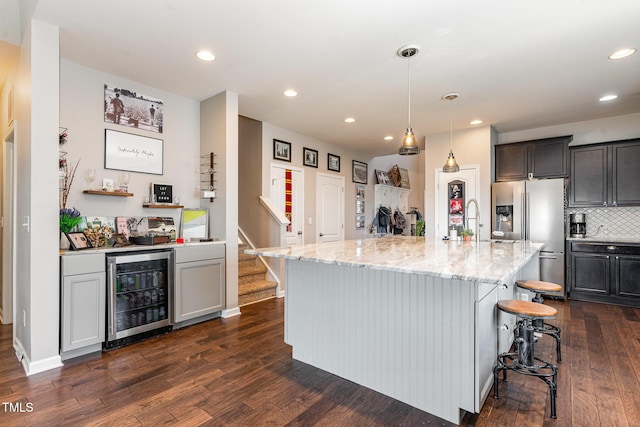 kitchen featuring light stone counters, beverage cooler, a breakfast bar, a center island with sink, and pendant lighting