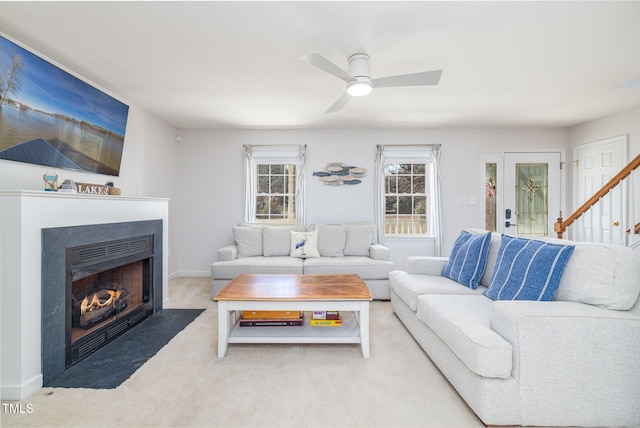 living room with stairway, a fireplace with flush hearth, light carpet, ceiling fan, and baseboards