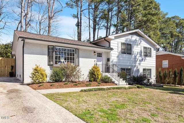 split level home featuring driveway, brick siding, a front yard, and fence