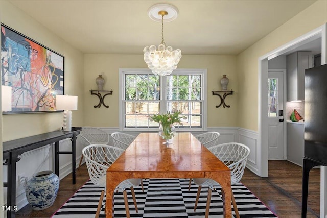 dining area with a wainscoted wall, dark wood-type flooring, and an inviting chandelier