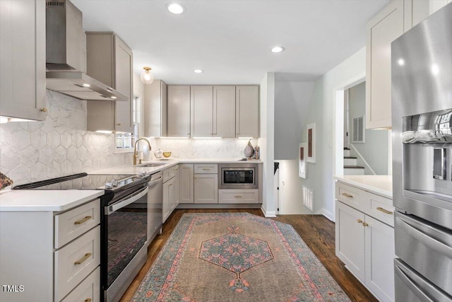 kitchen with dark wood finished floors, light countertops, appliances with stainless steel finishes, a sink, and wall chimney range hood