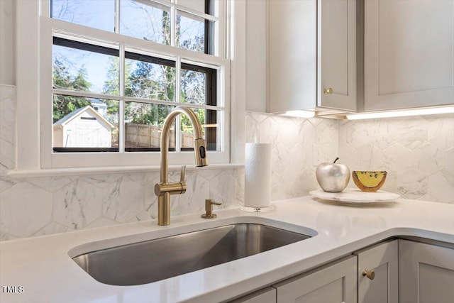 room details featuring light countertops, a sink, decorative backsplash, and white cabinetry