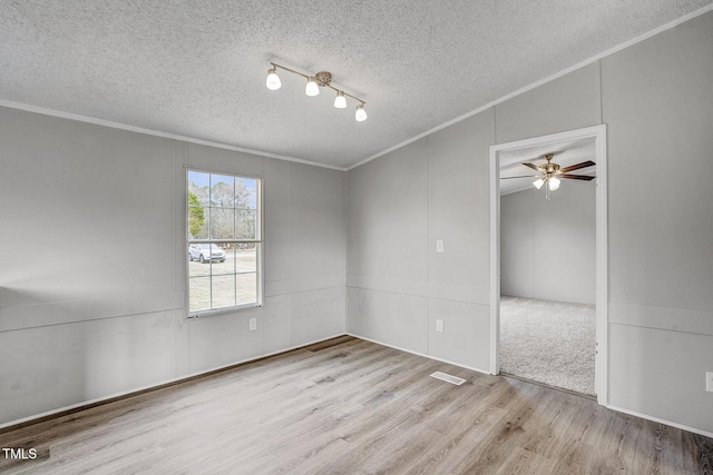 unfurnished room featuring a ceiling fan, a textured ceiling, ornamental molding, and wood finished floors