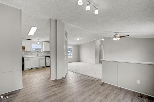 unfurnished living room with light wood-style flooring, vaulted ceiling, a textured ceiling, a sink, and ceiling fan