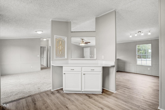 kitchen featuring white cabinets, light countertops, a textured ceiling, crown molding, and light wood-type flooring