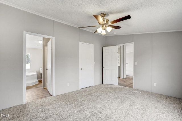 unfurnished bedroom with ceiling fan, ornamental molding, ensuite bathroom, a textured ceiling, and carpet flooring