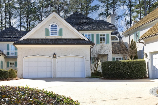 view of front facade with stucco siding, driveway, a chimney, and an attached garage