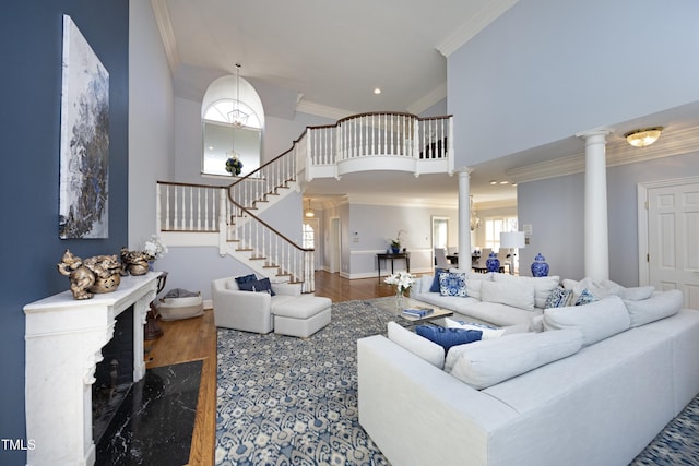 living room featuring wood finished floors, crown molding, decorative columns, a towering ceiling, and stairs