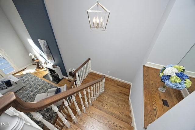 staircase with a notable chandelier, wood finished floors, and baseboards