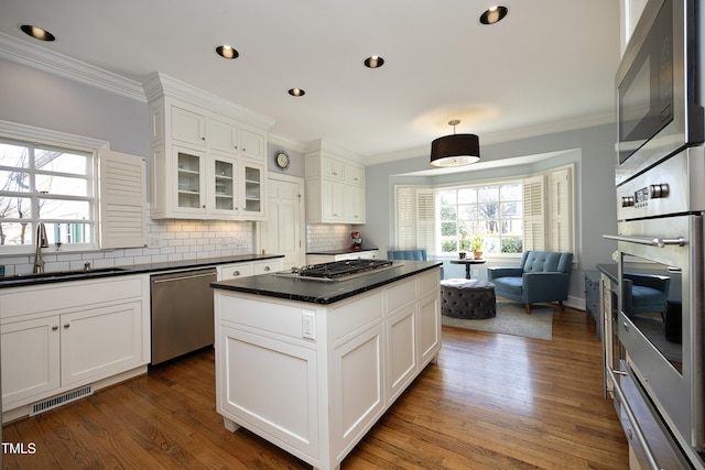 kitchen featuring visible vents, a sink, dark countertops, stainless steel appliances, and crown molding