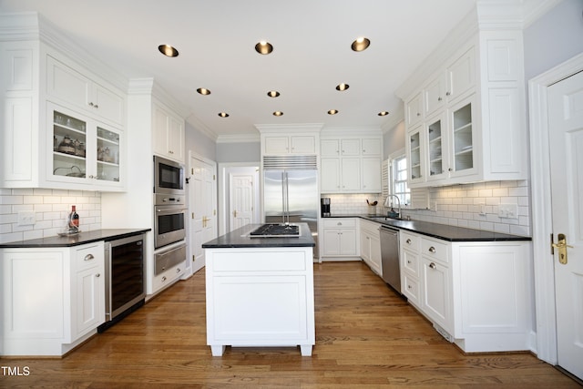 kitchen featuring dark countertops, wine cooler, built in appliances, and a sink