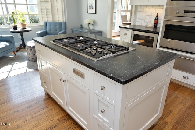 kitchen with a kitchen island, tasteful backsplash, white cabinetry, light wood-style floors, and appliances with stainless steel finishes