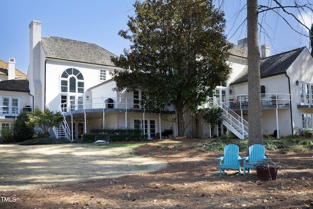 back of house with stucco siding, a chimney, and stairs