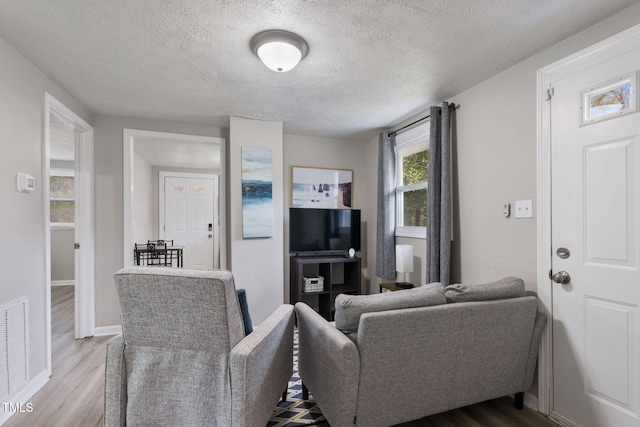 living room with visible vents, baseboards, a textured ceiling, and wood finished floors