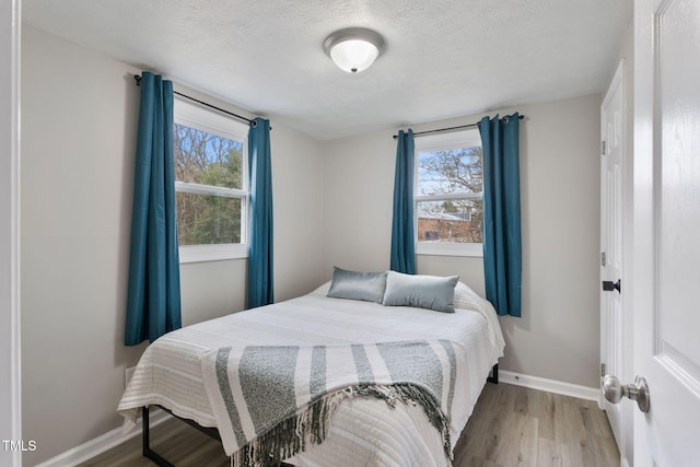 bedroom with multiple windows, a textured ceiling, baseboards, and wood finished floors