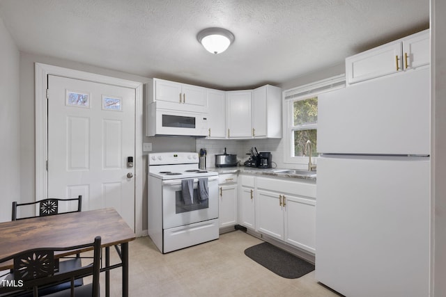 kitchen featuring white appliances, white cabinets, light floors, and a sink