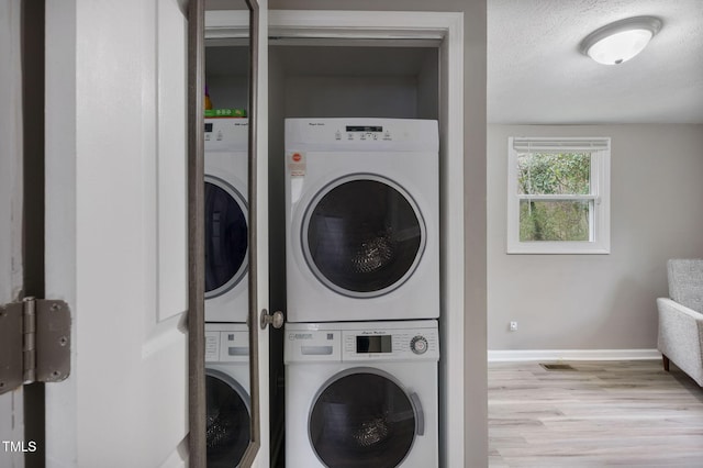 washroom featuring baseboards, laundry area, stacked washing maching and dryer, wood finished floors, and a textured ceiling