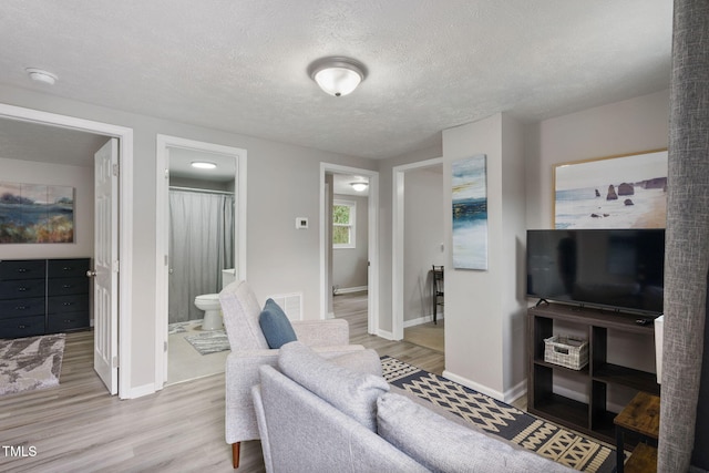 living room with visible vents, a textured ceiling, baseboards, and wood finished floors