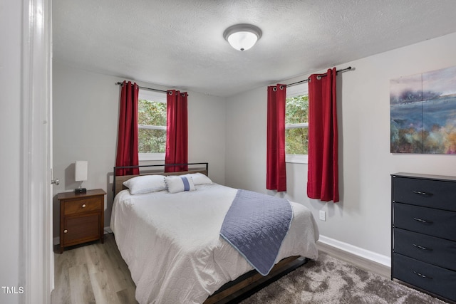 bedroom with light wood-style flooring, a textured ceiling, and multiple windows