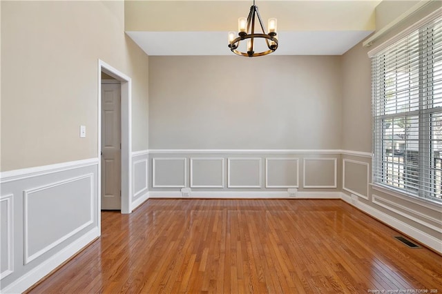 empty room with visible vents, a notable chandelier, a decorative wall, and hardwood / wood-style flooring