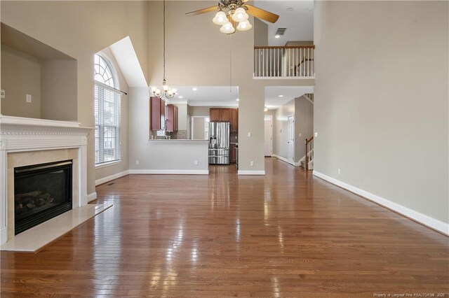 147 Lamplighter Way, Spring Lake, NC 28390 - unfurnished living room featuring baseboards, a fireplace, dark wood-style floors, a high ceiling, and ceiling fan with notable chandelier