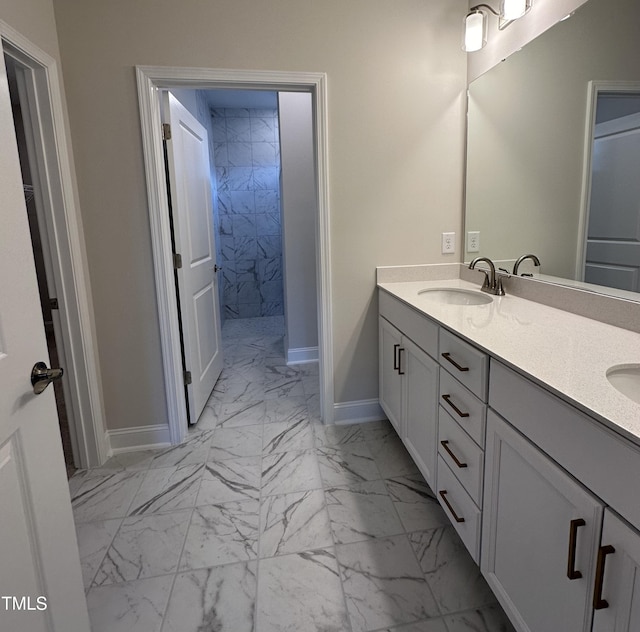 full bath featuring a tile shower, double vanity, marble finish floor, a sink, and baseboards