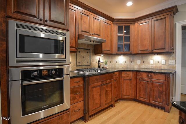 kitchen featuring tasteful backsplash, light wood-style floors, dark stone countertops, stainless steel appliances, and under cabinet range hood