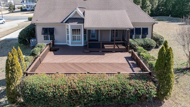 rear view of property with a deck, roof with shingles, and a sunroom