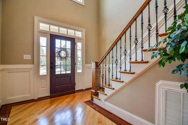 foyer with visible vents, a decorative wall, a towering ceiling, wainscoting, and light wood-type flooring