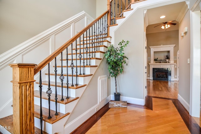 stairs with visible vents, ornamental molding, a high end fireplace, ceiling fan, and wood finished floors